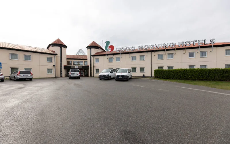 Hotellfasad med logotyp och parkeringsplats framför byggnaden.