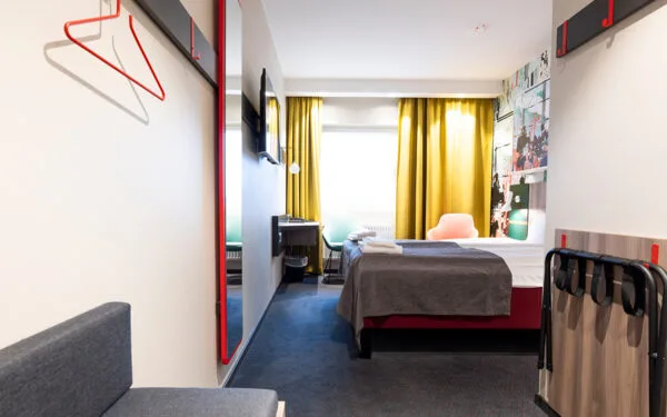 Hotellrum med dubbelsäng, gula gardiner och färgglada fåtöljer.