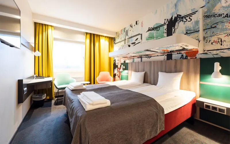 Hotellrum med bäddad dubbelsäng och en bäddad extrasäng ovanför dubbelsängen.