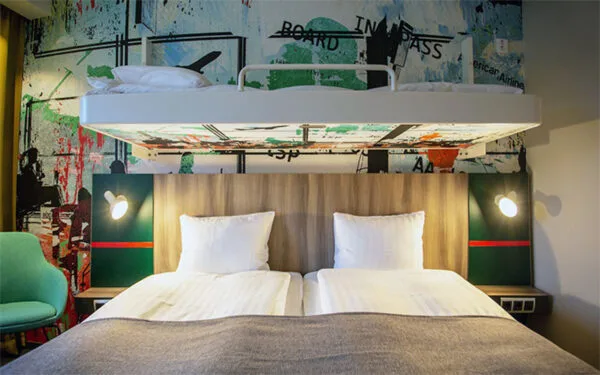 Hotellrum med dubbelsäng och väggfast extrasäng ovanför.