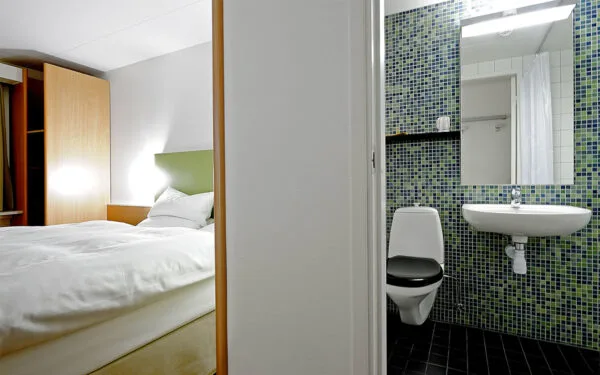 Hotellrum med säng och angränsande badrum med toalett.