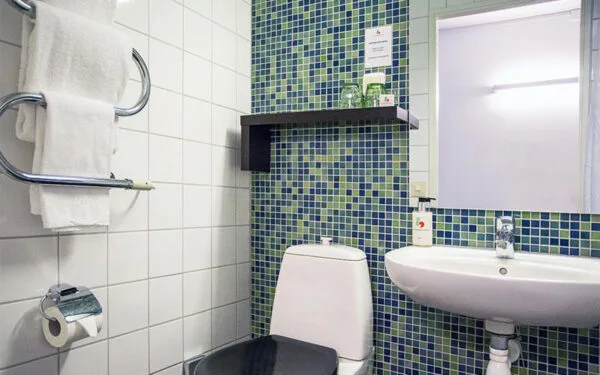 Hotellbadrum med toalett, handfat och blågrönt kakel.