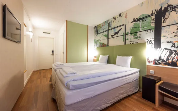 Hotellrum med dubbelsäng, grön väggpanel och trägolv.