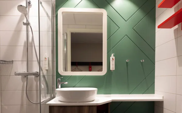 Hotellbadrum med spegel, handfat och grönt kakel.