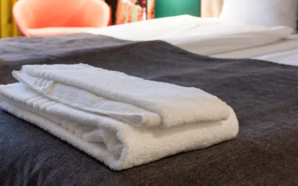 Hopvikt vit handduk liggande på grå filt i hotellrum.