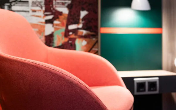 Närbild på röd fåtölj och vägglampa i hotellrum.