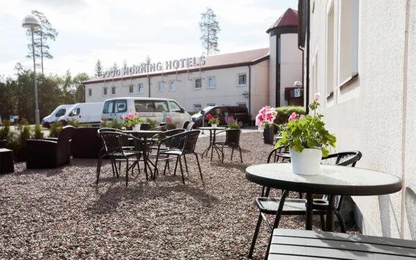 Uteservering med bord, stolar och blomkrukor utanför hotellbyggnad.