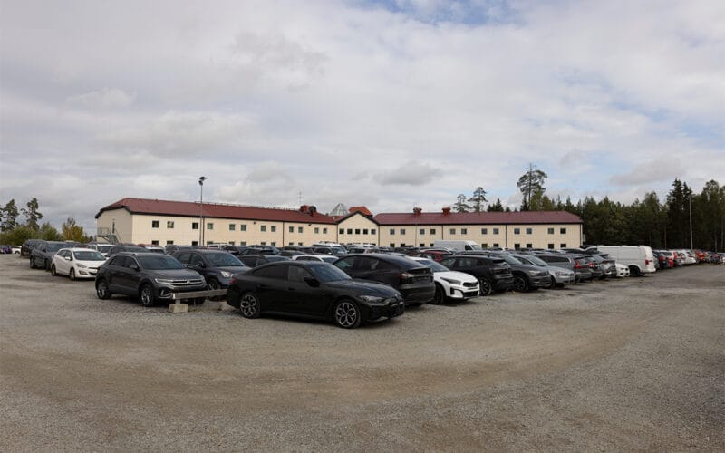 Stor parkeringsplats med flera bilar framför hotellbyggnad.