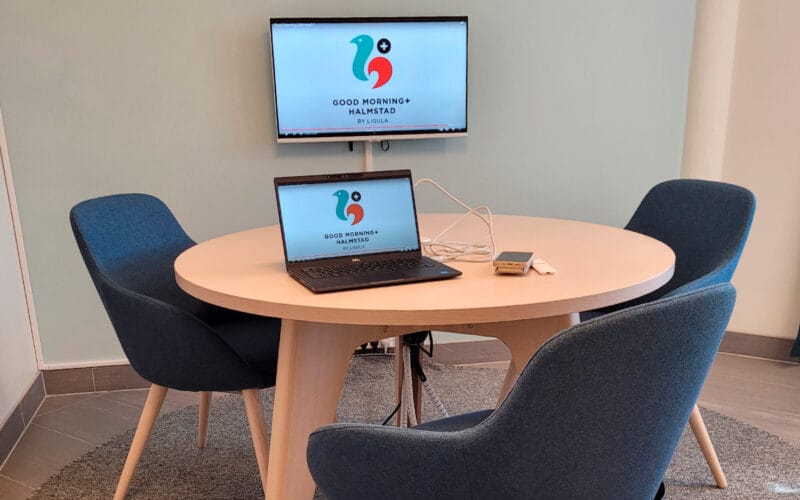 Mötesrum med runt bord, fyra stolar och skärm för presentation.
