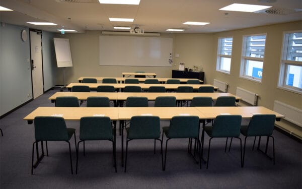 Konferensrum med gröna stolar i rader framför projektorduk