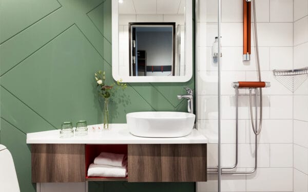Hotellbadrum med spegel, handfat och grön kakelvägg.