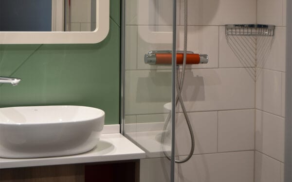 Närbild på handfat och dusch med grönt kakel.