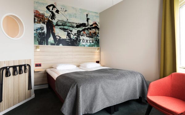 Bäddad dubbelsäng med sänggavel i trä och färgglad väggmålning.