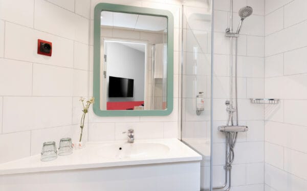 Hotellbadrum med spegel, handfat och dusch.