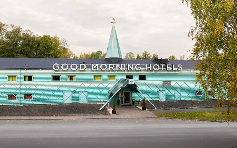 Hotellfasad i grönt med entré och Good Morning Hotels logotyp.