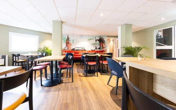 Restaurang med trägolv, färgglada stolar och väggmålning.