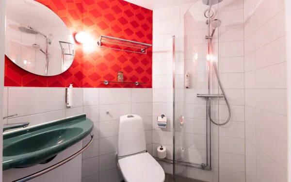 Hotellbadrum med vitt kakel, röd fondvägg och dusch.
