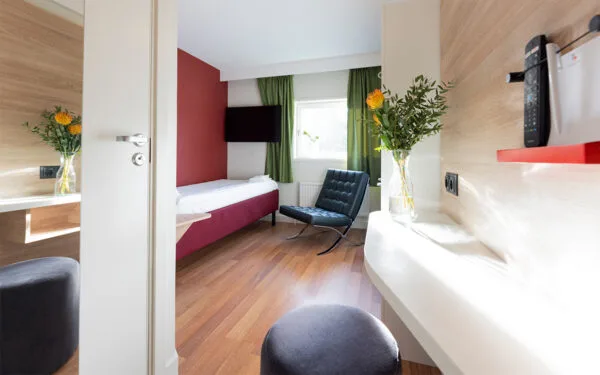 Hotellrum med enkelsäng, vita väggar och trägolv.