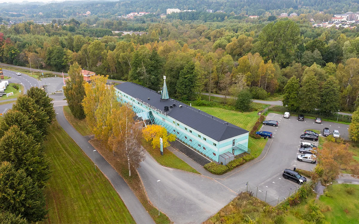 Luftfoto af hotelbygning omgivet af grønne områder og parkeringspladser.