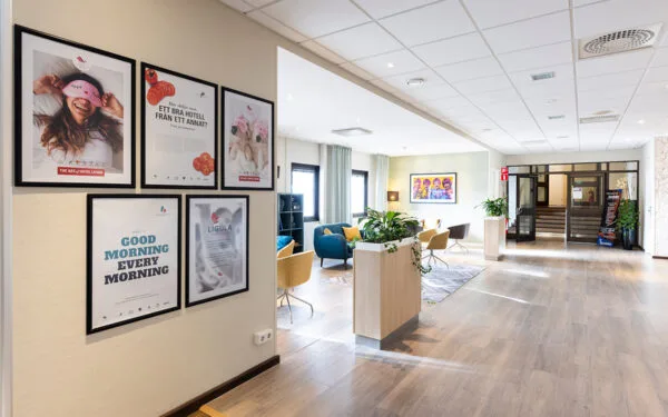 Hotellkorridor med affischer på väggen och en loungehörna längre in.