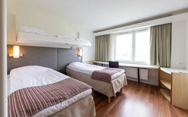 Hotellrum med två enkelsängar och en nedfällbar väggsäng ovanför, samt skrivbord vid fönster.