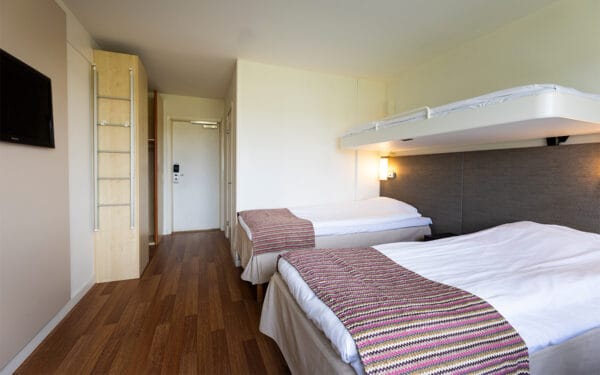 Hotellrum med två sängar, TV och nedfällbar säng på väggen.