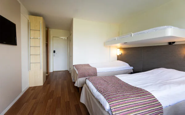 Hotellrum med två sängar, TV och nedfällbar säng på väggen.