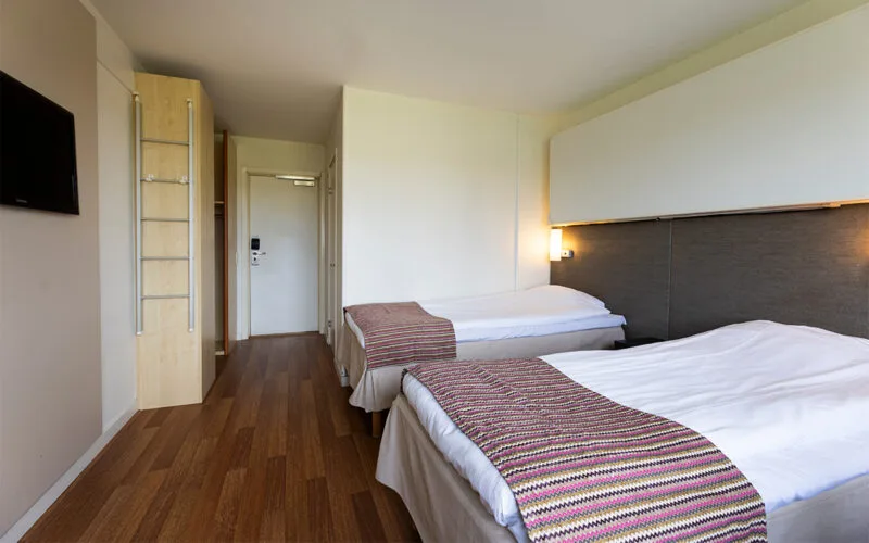 Hotellrum med två enkelsängar och TV på väggen