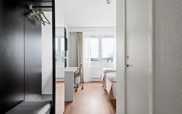 Hotellrum med två sängar, skrivbord och stora fönster med utsikt.