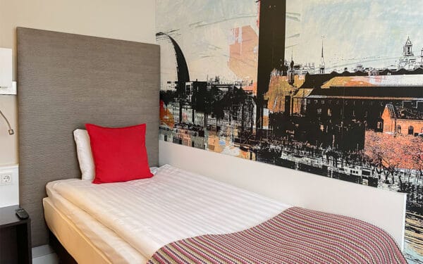 Hotellrum med enkelsäng, väggmålning och röda kuddar.