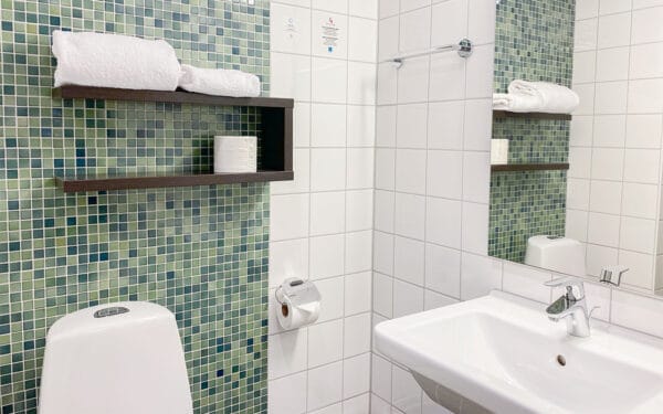 Badrum med vitt kakel, grön mosaik, toalett och handfat.