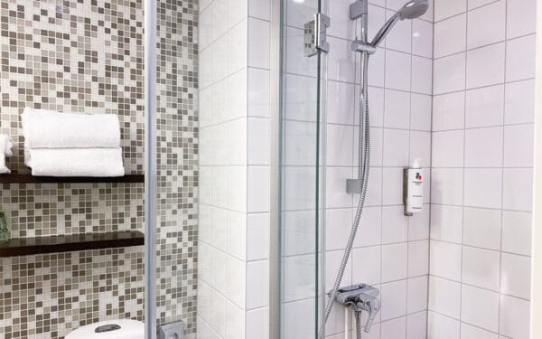 Hotellbadrum med dusch, glasvägg och kaklade väggar.