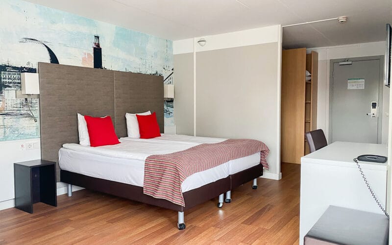 Hotellrum med dubbelsäng, röda kuddar och trägolv.