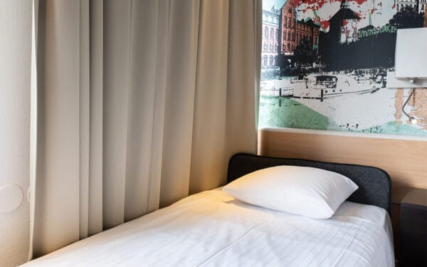 Hotellrum med enkelsäng, tavla och gardiner.