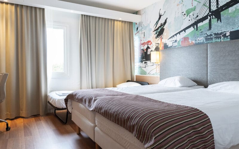 Hotellrum med två enkelsängar och ljus inredning.