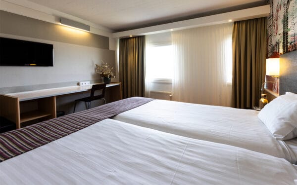 Hotellrum med dubbelsäng, tavlor och sänglampor.