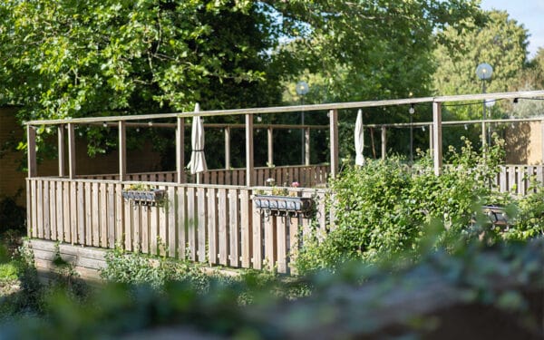 Uteservering/terrass med sittplatser omgiven av grönska.