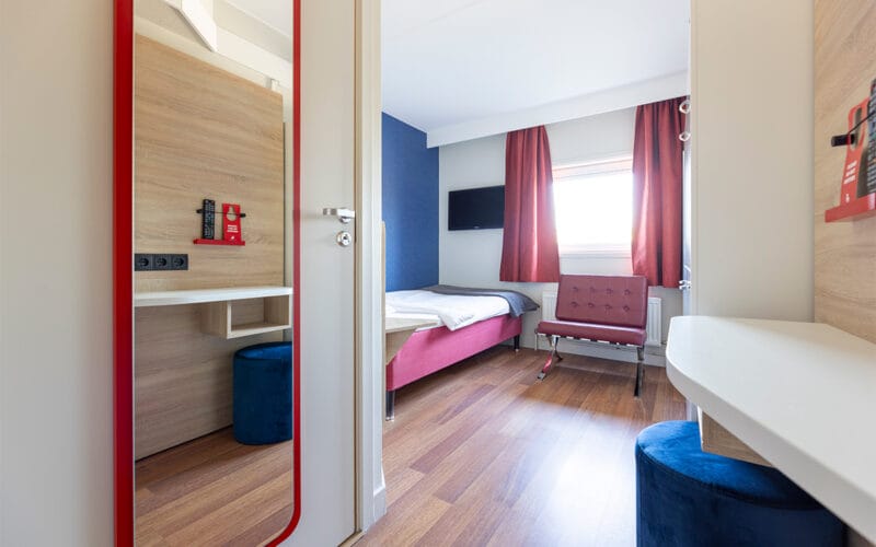 Hotellrum med säng, röda gardiner och trädetaljer.