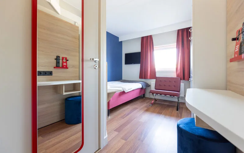 Hotellrum med säng, röda gardiner och trädetaljer.