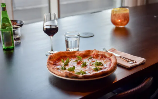 Pizza och vinglas på högt bord i baren på Restaurang Angelini