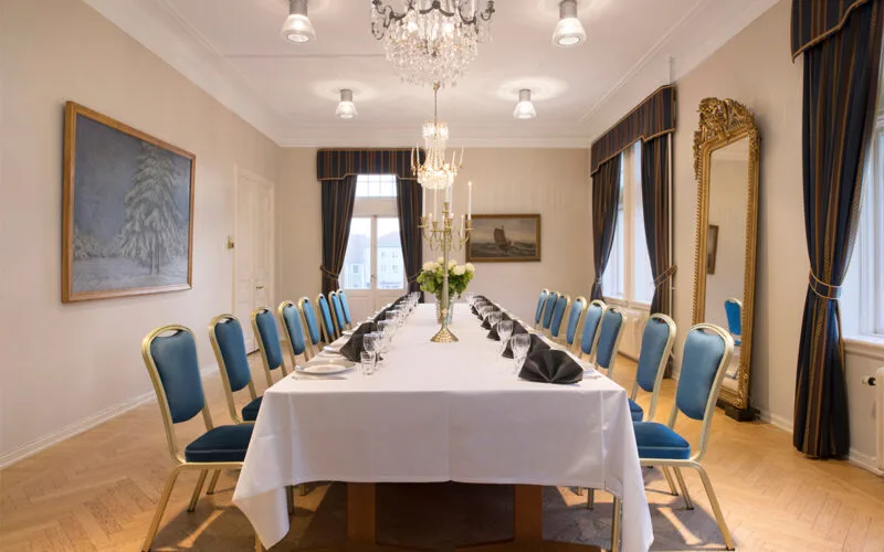 Salong med långbord, blå stolar och kristallkrona