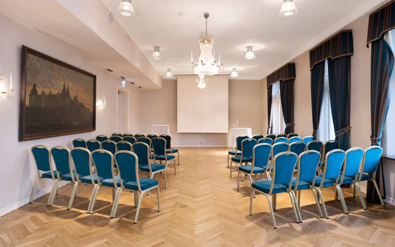 Konferens och festsal med blå stolar, parkettgolv och projektorduk