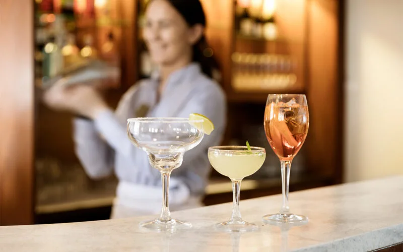Servitris som häller upp tre färgglada cocktails på bardisk.