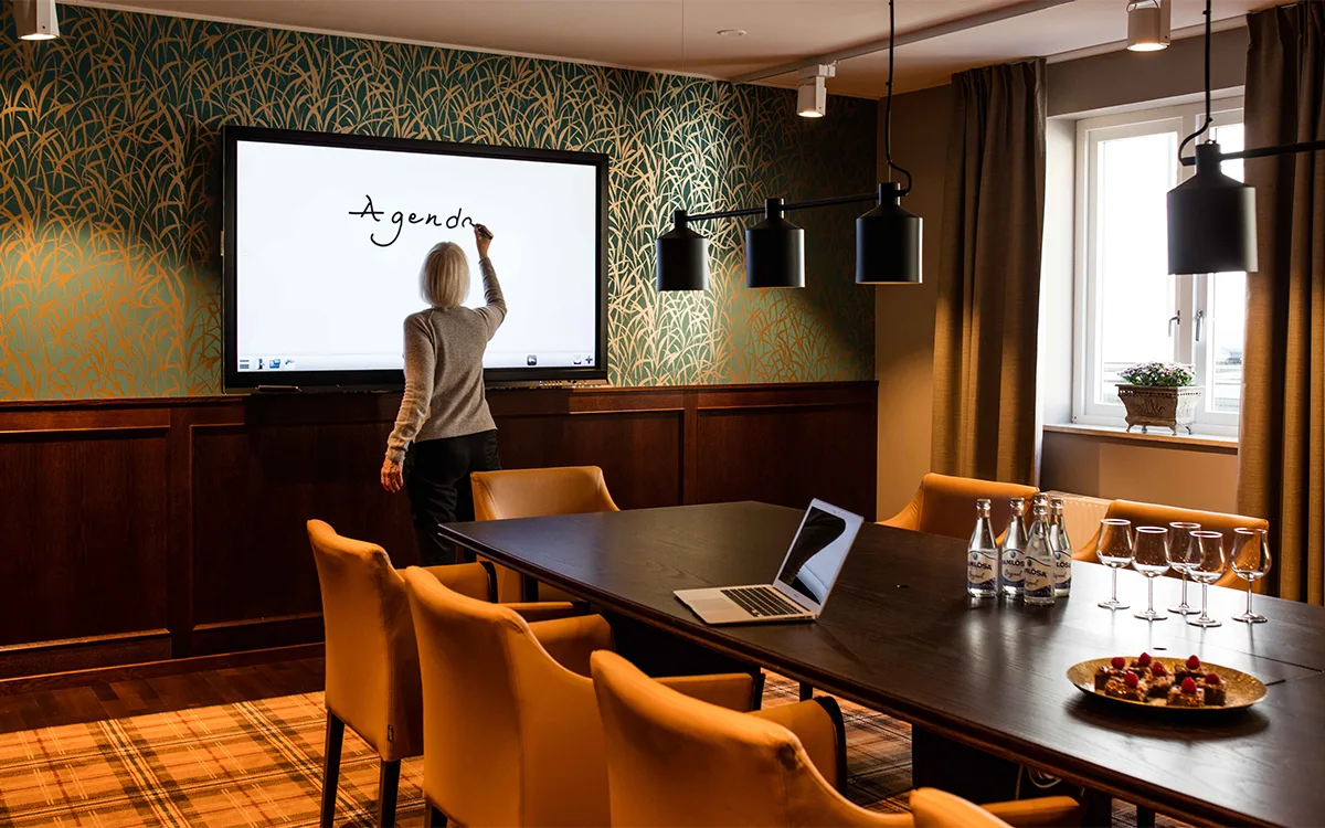 Ett mötesrum med digital whiteboard, stolar och bord dukat för möte.