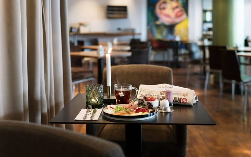 Dukat bord med frukostservering, tända ljus och tidning i hotellrestaurang