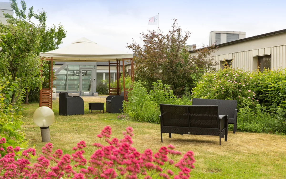 Frodig hotelhave med siddepladser og pavillon.