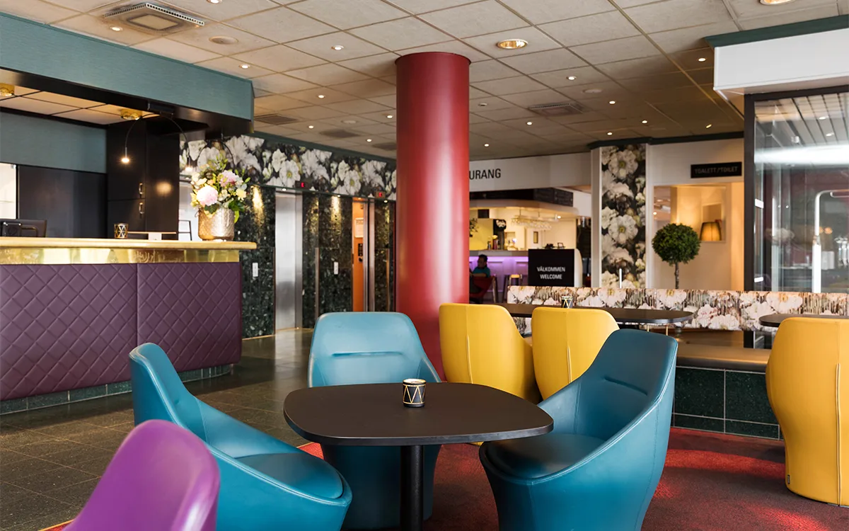 Hotellobby med färgglada stolar, reception och blommiga väggdetaljer