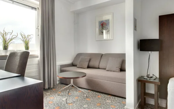 Hotellrum med bäddsoffa och soffbord i ljus inredning.