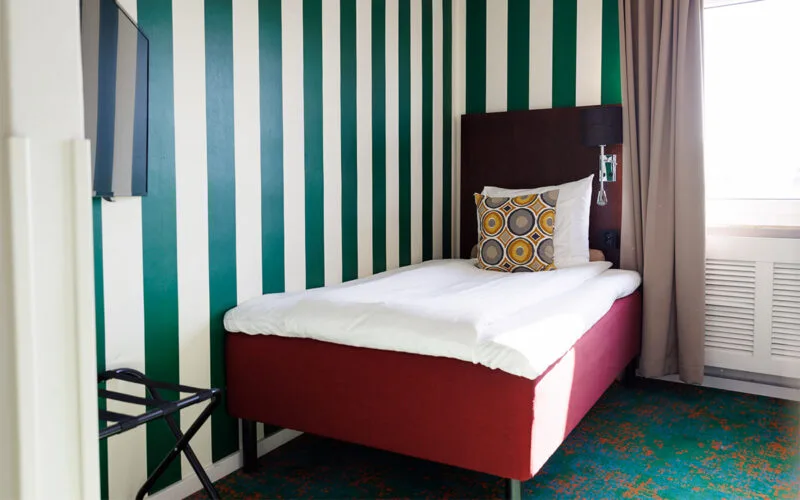 Hotellrum med enkelsäng, randig fondvägg och prydnadskudde