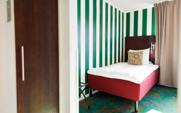 Enkelsäng i rum med randig vägg och grön heltäckningsmatta